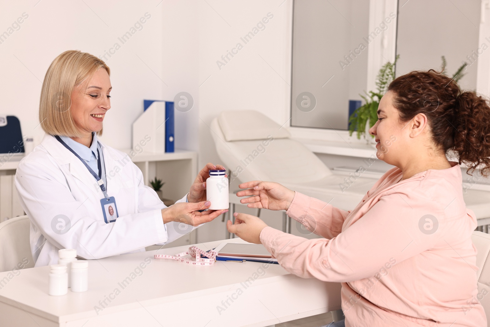 Photo of Weight loss. Smiling nutritionist giving medical bottle with pills to patient at table in clinic