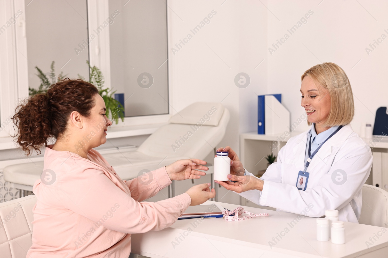 Photo of Weight loss. Smiling nutritionist giving medical bottle with pills to patient at table in clinic