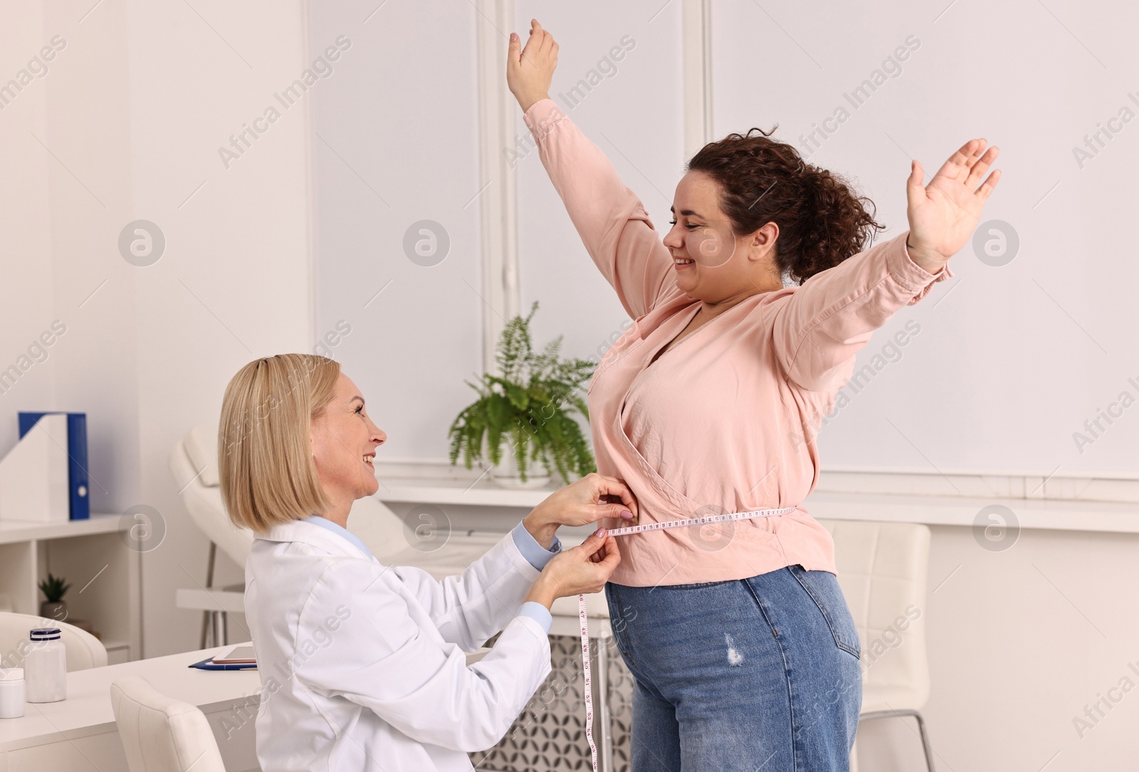 Photo of Happy woman lost weight. Smiling nutritionist measuring patient's waist with tape in clinic