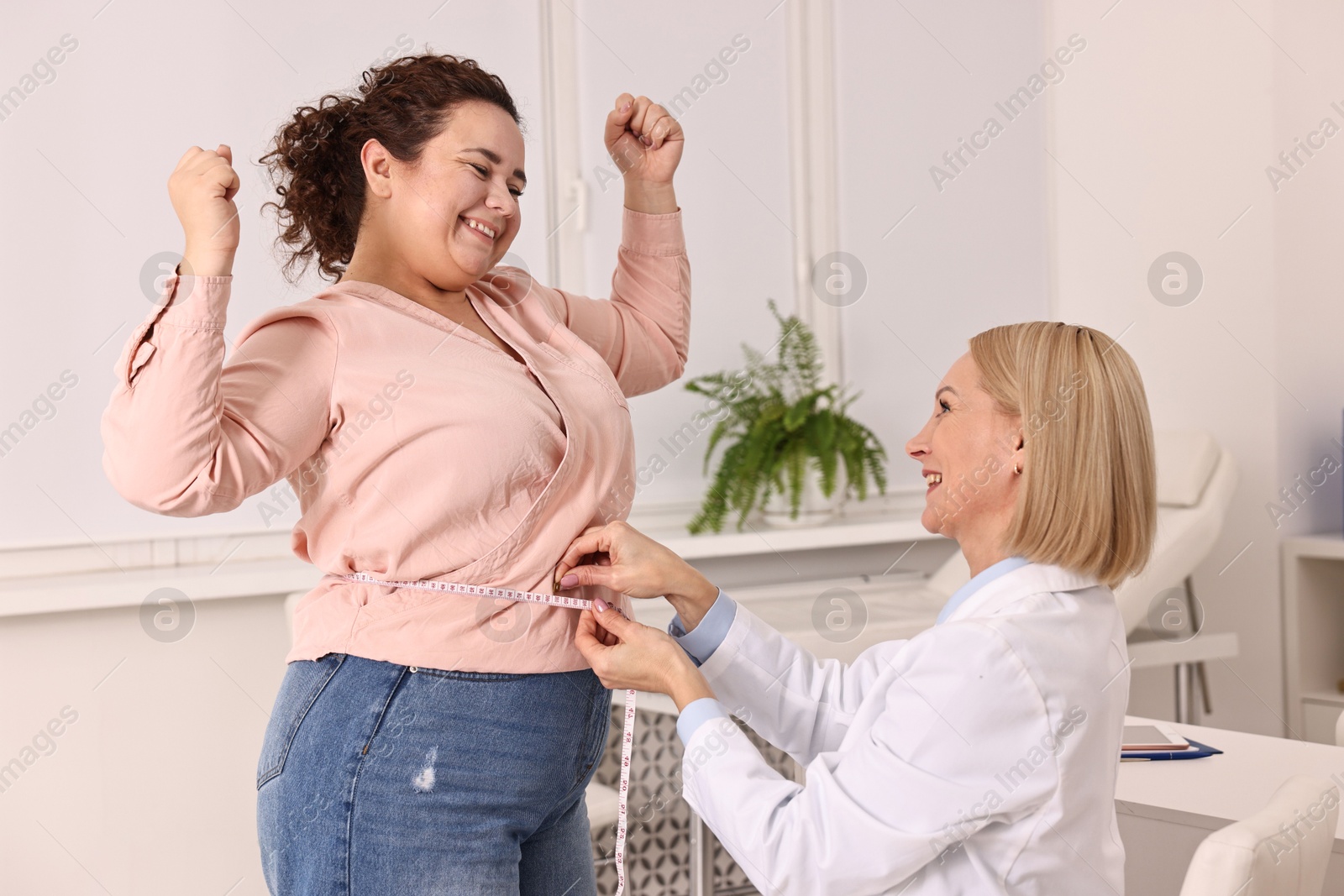 Photo of Happy woman lost weight. Smiling nutritionist measuring patient's waist with tape in clinic