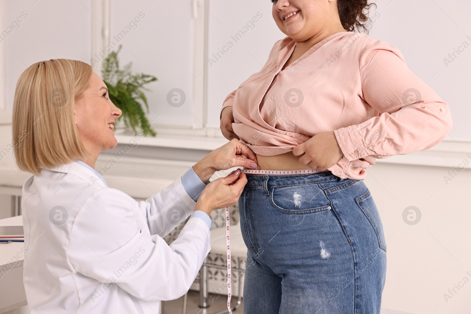 Photo of Happy woman lost weight. Nutritionist measuring patient's waist with tape in clinic