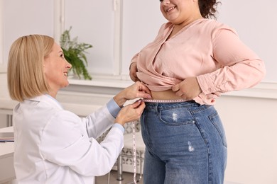 Photo of Happy woman lost weight. Nutritionist measuring patient's waist with tape in clinic