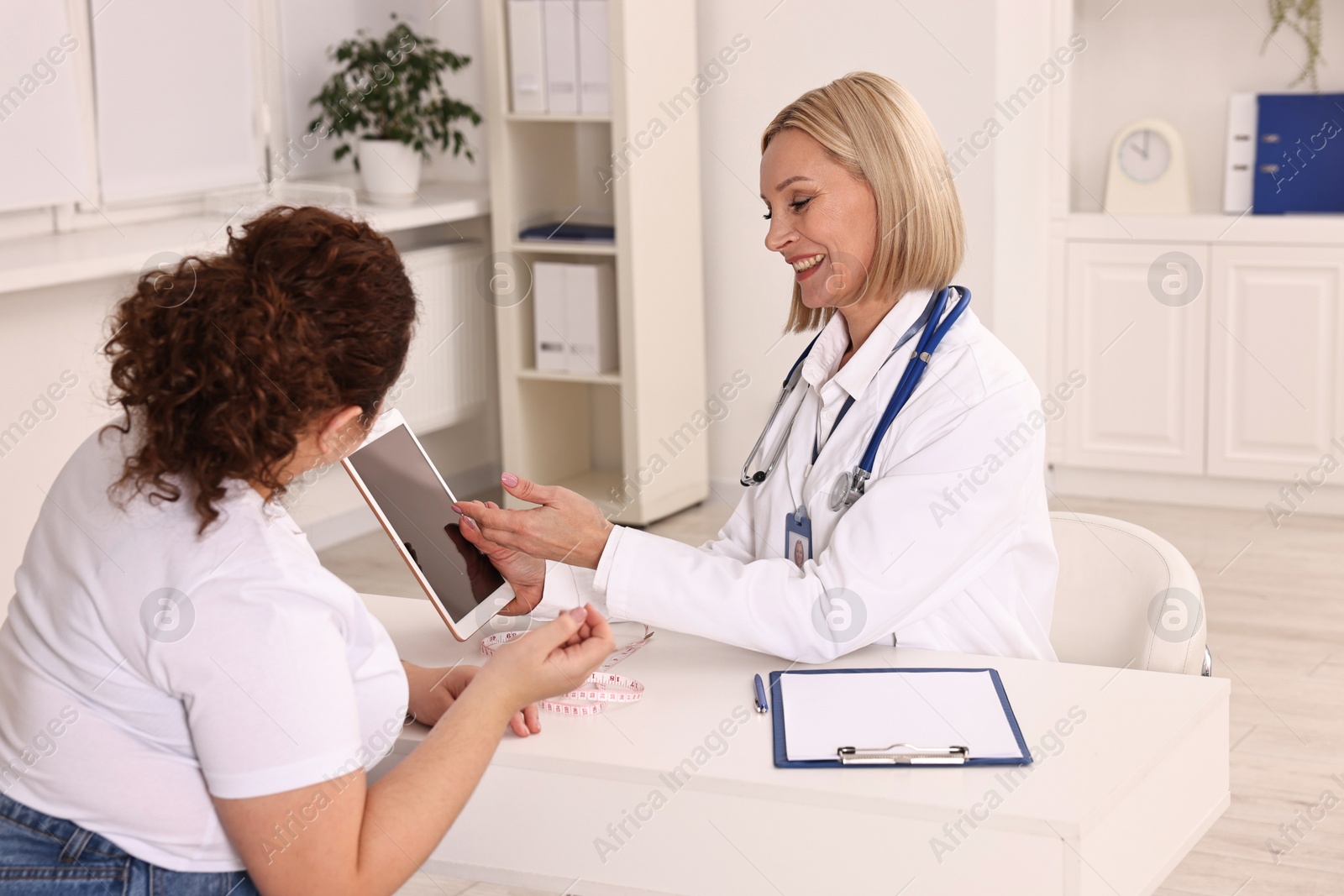 Photo of Weight loss. Smiling nutritionist with tablet consulting patient at table in clinic