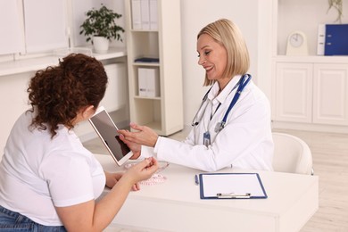 Photo of Weight loss. Smiling nutritionist with tablet consulting patient at table in clinic