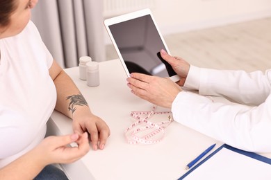 Photo of Weight loss. Nutritionist with tablet consulting patient at table in clinic, closeup