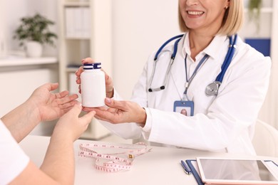 Photo of Weight loss. Smiling nutritionist giving medical bottle with pills to patient at table in clinic, closeup