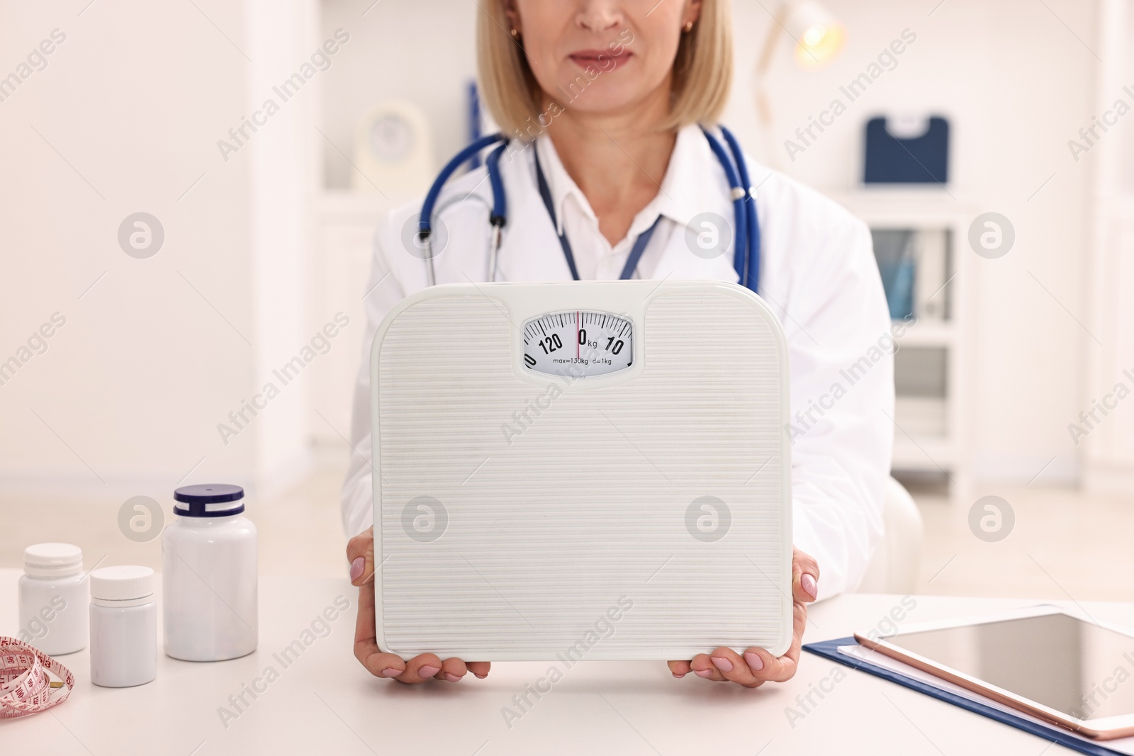 Photo of Weight loss. Nutritionist with scales at table in clinic, closeup