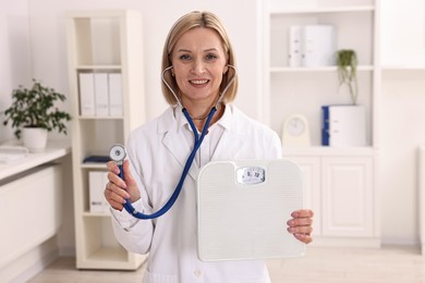 Photo of Weight loss. Smiling nutritionist with stethoscope and scales in clinic