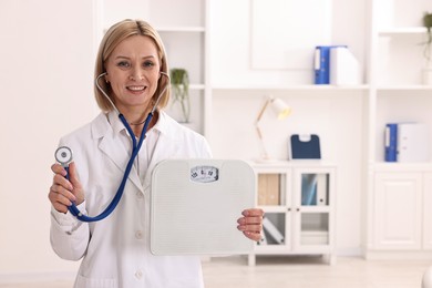 Photo of Weight loss. Smiling nutritionist with stethoscope and scales in clinic. Space for text