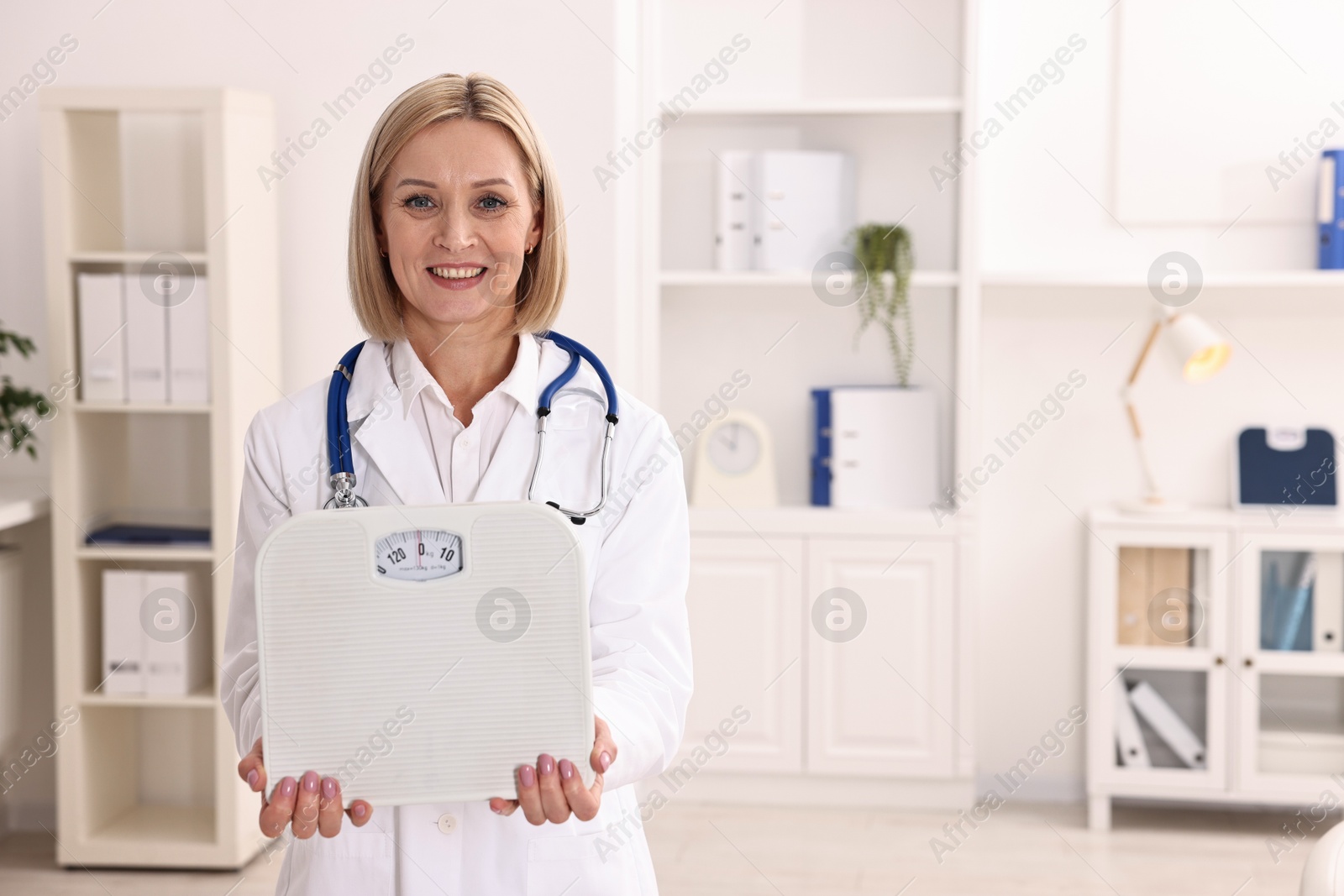 Photo of Weight loss. Smiling nutritionist with stethoscope and scales in clinic. Space for text