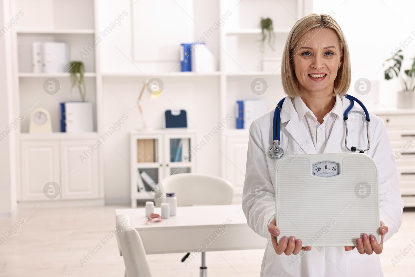 Photo of Weight loss. Smiling nutritionist with stethoscope and scales in clinic. Space for text