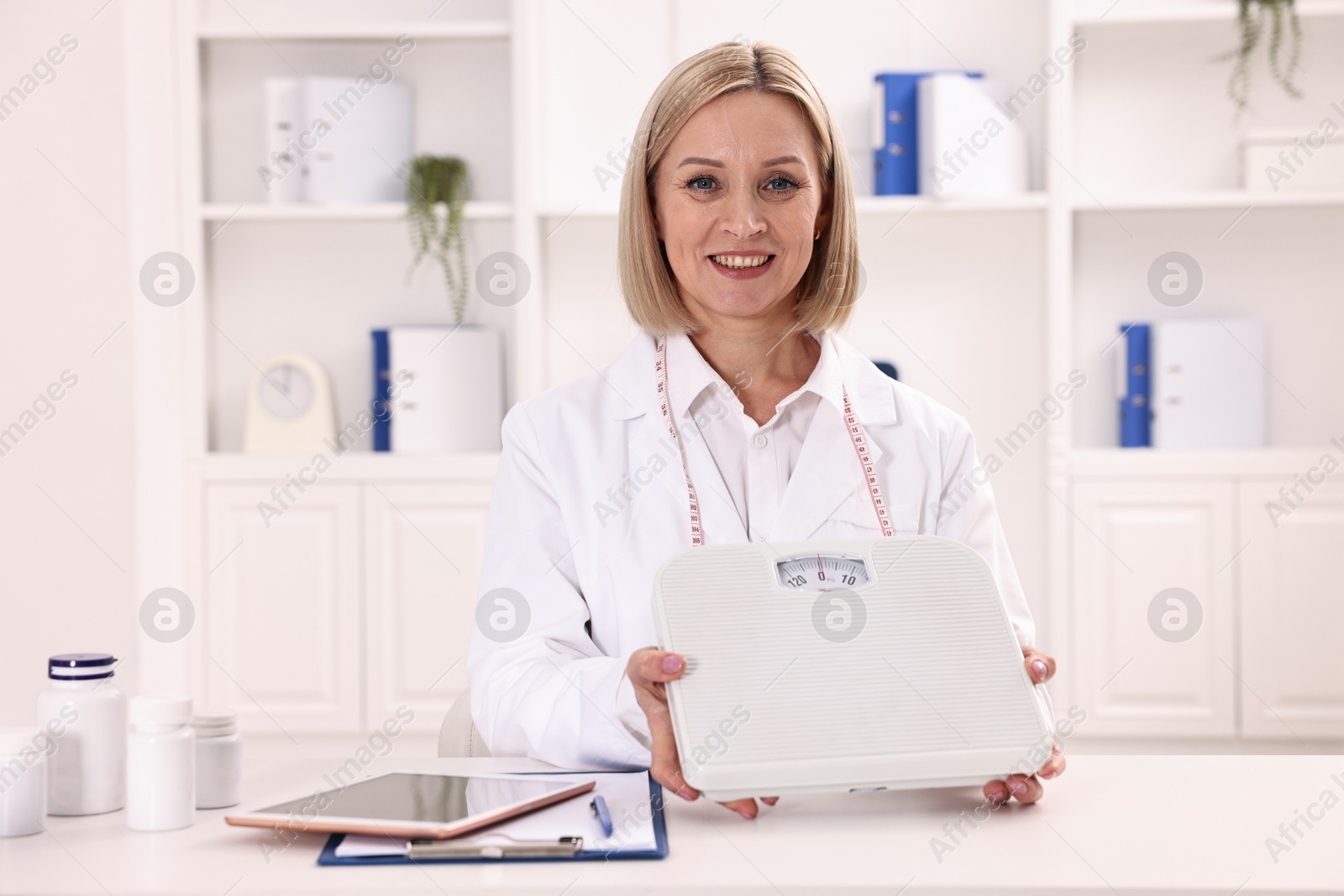 Photo of Weight loss. Smiling nutritionist with scales at table in clinic