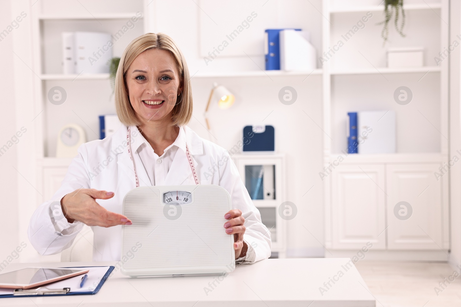 Photo of Weight loss. Smiling nutritionist with scales at table in clinic, space for text