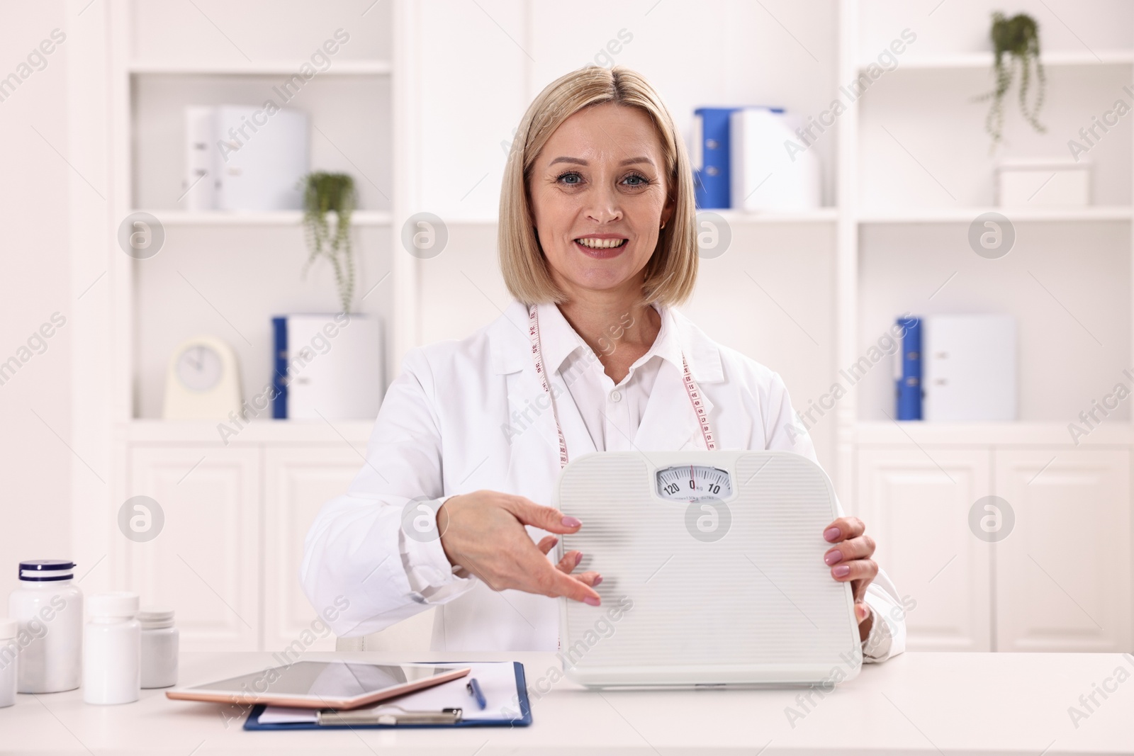 Photo of Weight loss. Smiling nutritionist with scales at table in clinic