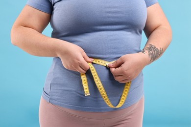 Photo of Weight loss. Plus size woman measuring waist with tape on light blue background, closeup