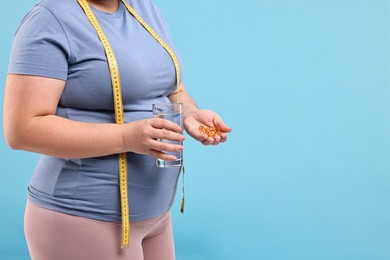 Photo of Plus size woman holding pile of weight loss supplements and glass with water on light blue background, closeup. Space for text