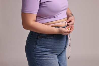 Photo of Plus size woman measuring waist with tape and holding pile of weight loss supplements on grey background, closeup