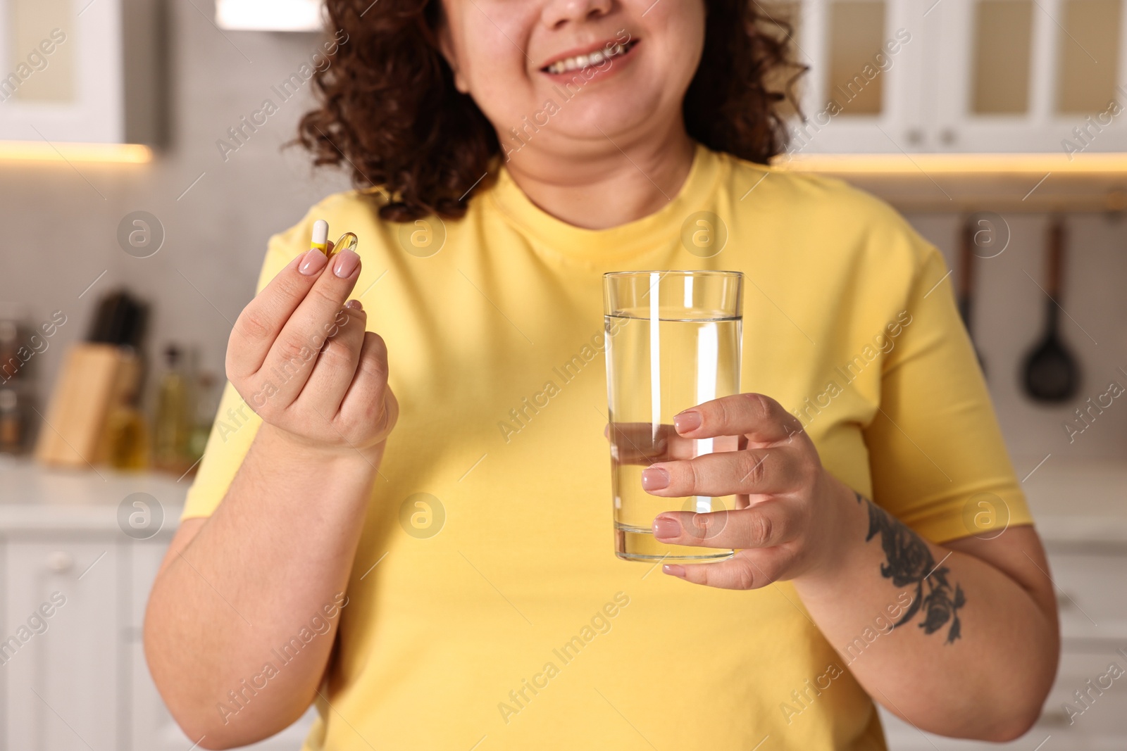 Photo of Happy plus size woman with weight loss supplements and glass of water in kitchen, closeup