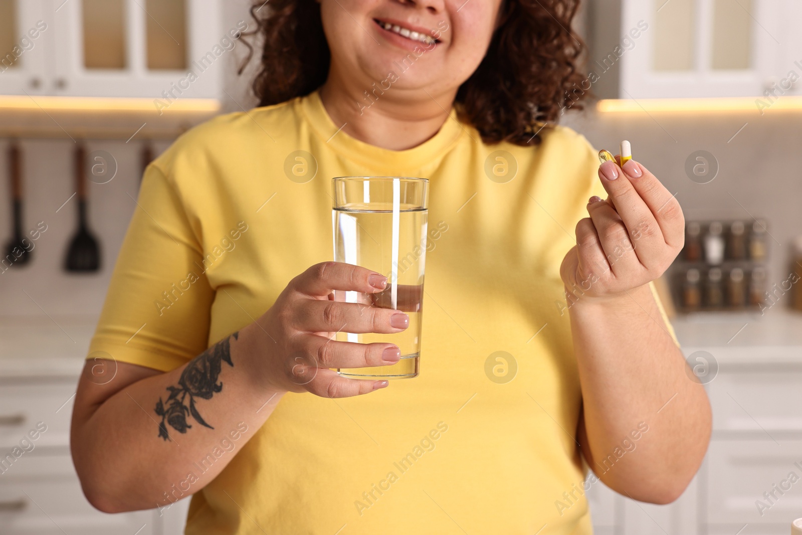 Photo of Happy plus size woman with weight loss supplements and glass of water in kitchen, closeup