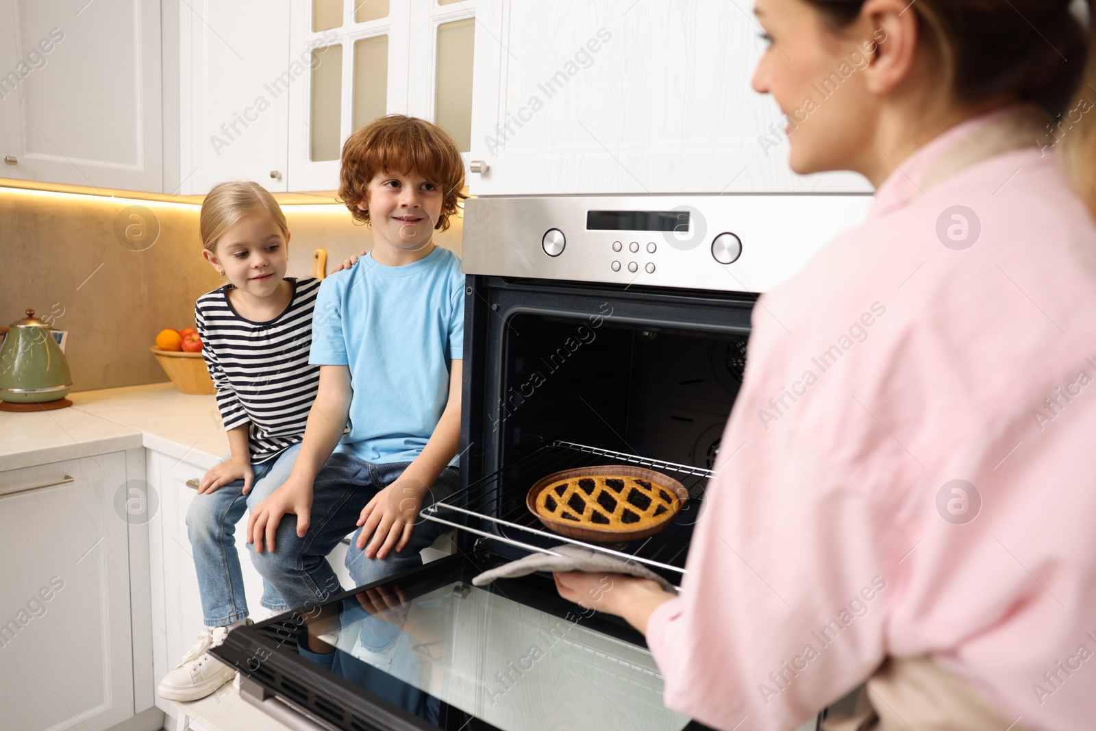 Photo of Mother and her kids taking out pie from oven in kitchen