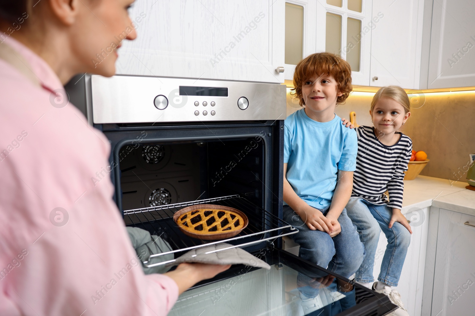 Photo of Mother and her kids taking out pie from oven in kitchen, closeup