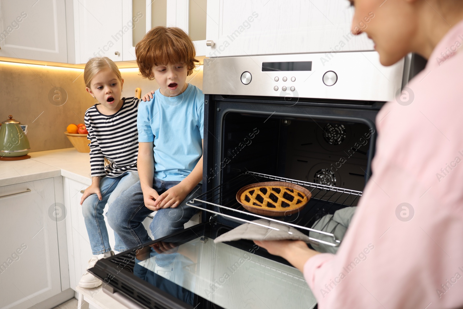 Photo of Mother and her kids taking out pie from oven in kitchen, closeup