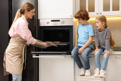 Photo of Mother and her kids taking out pie from oven in kitchen