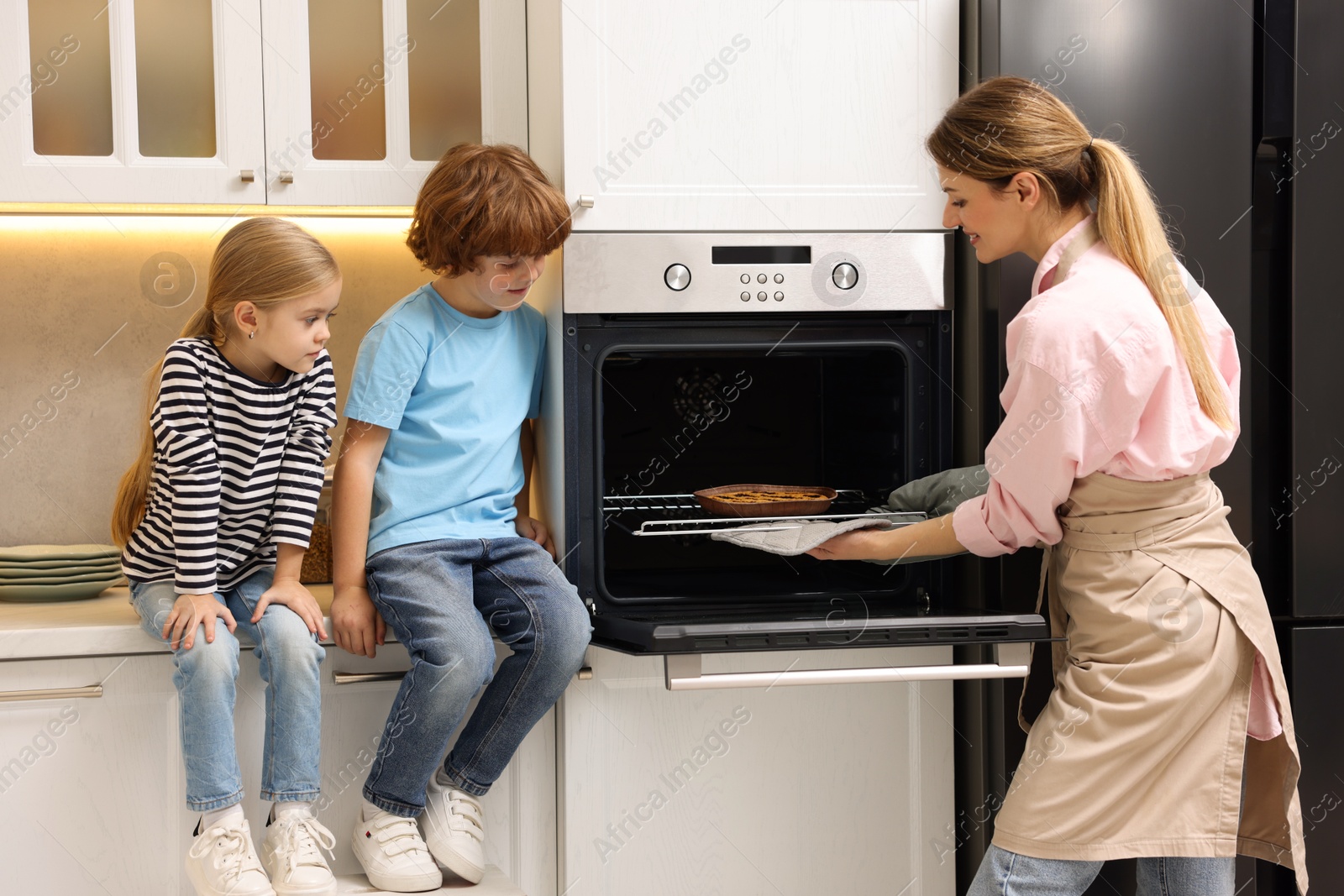 Photo of Mother and her kids taking out pie from oven in kitchen