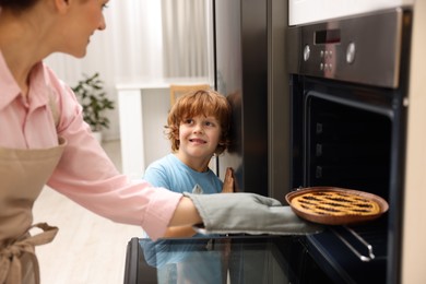 Photo of Mother and her son taking out pie from oven in kitchen, closeup