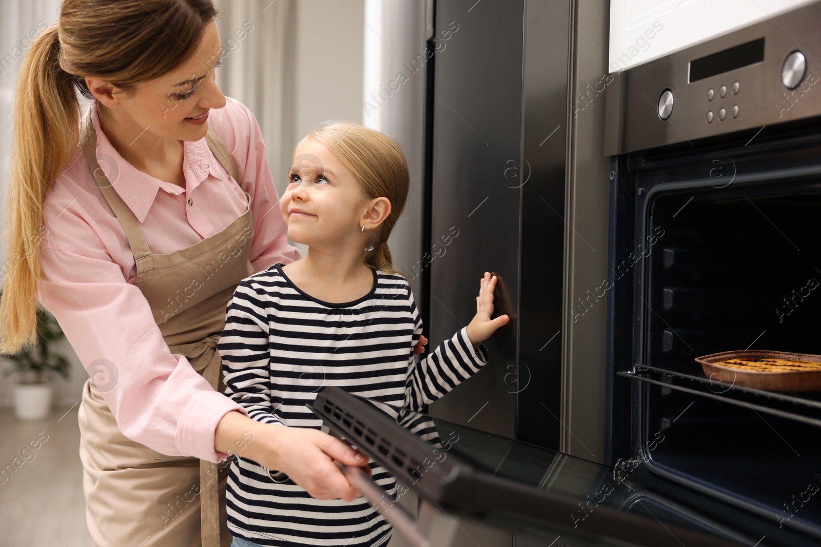 Photo of Mother and her daughter baking pie in oven indoors