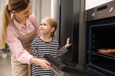 Photo of Mother and her daughter baking pie in oven indoors