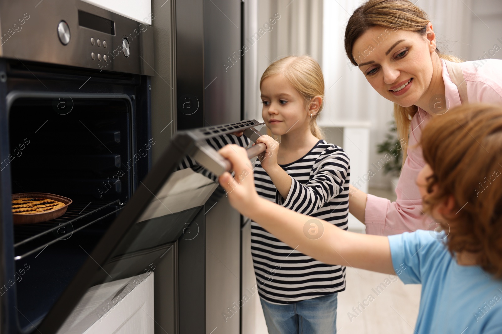 Photo of Mother and her kids baking pie in oven indoors