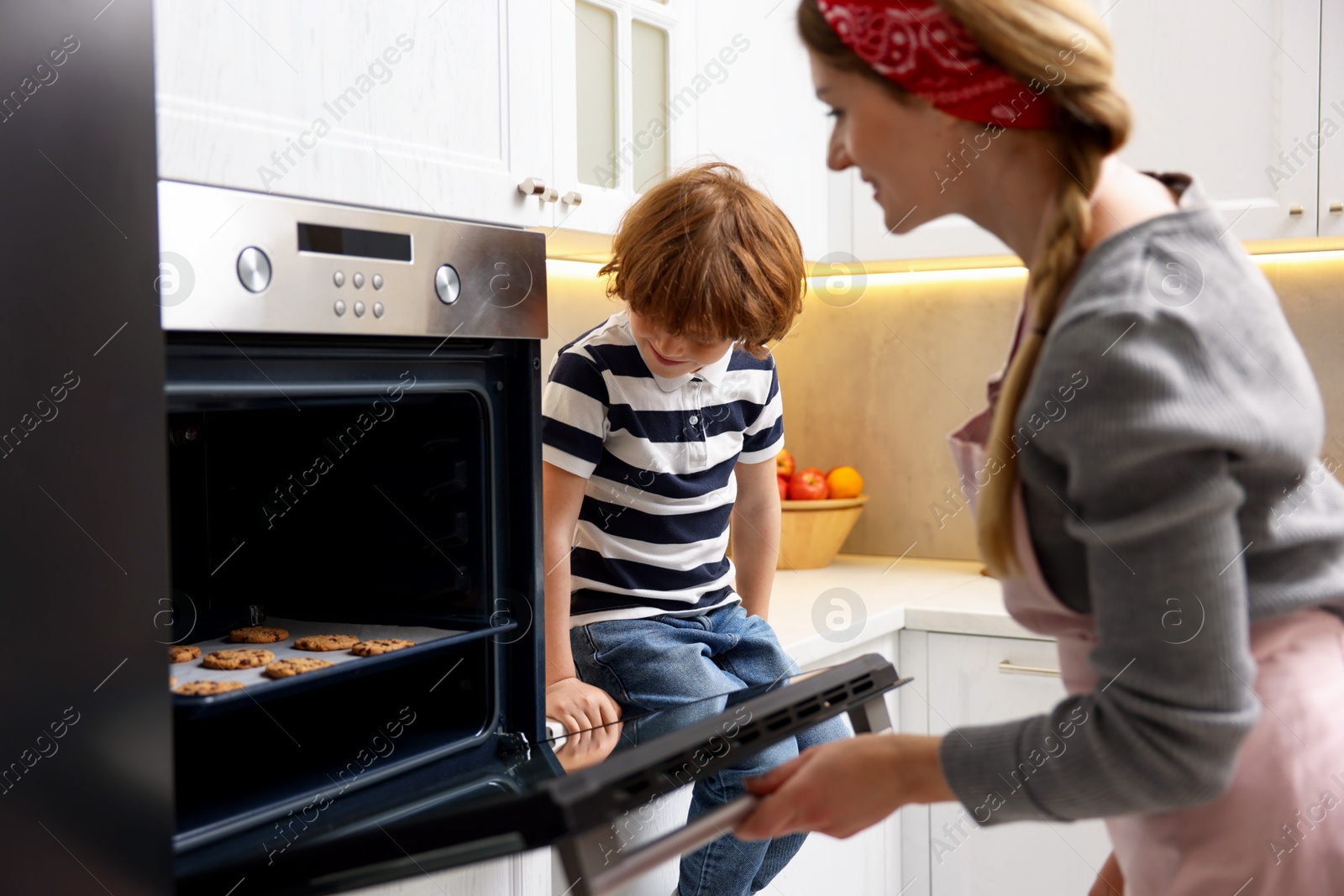 Photo of Mother and her son baking cookies in oven indoors