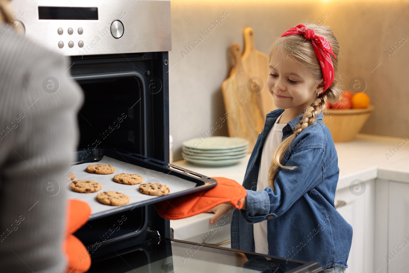 Photo of Mother and her daughter taking out buns from oven in kitchen, closeup