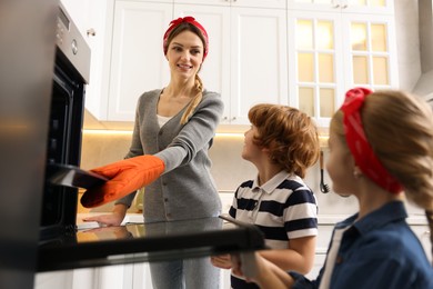 Photo of Mother and her kids taking out baking pan from oven in kitchen