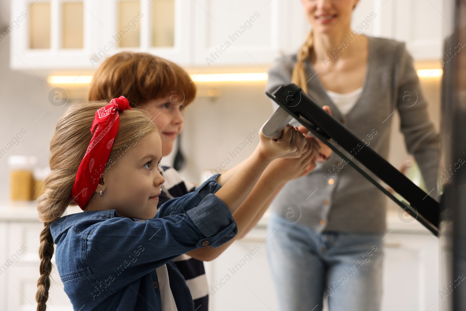 Photo of Mother and her children baking pastry in oven indoors, closeup