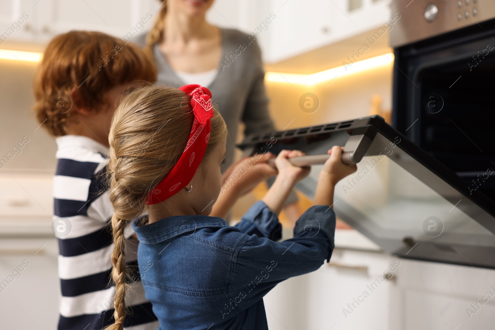 Photo of Mother and her children baking pastry in oven indoors, closeup