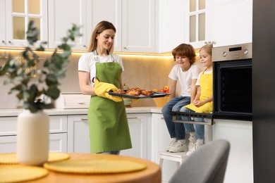 Photo of Happy mother holding baking pan with tasty buns near her kids in kitchen