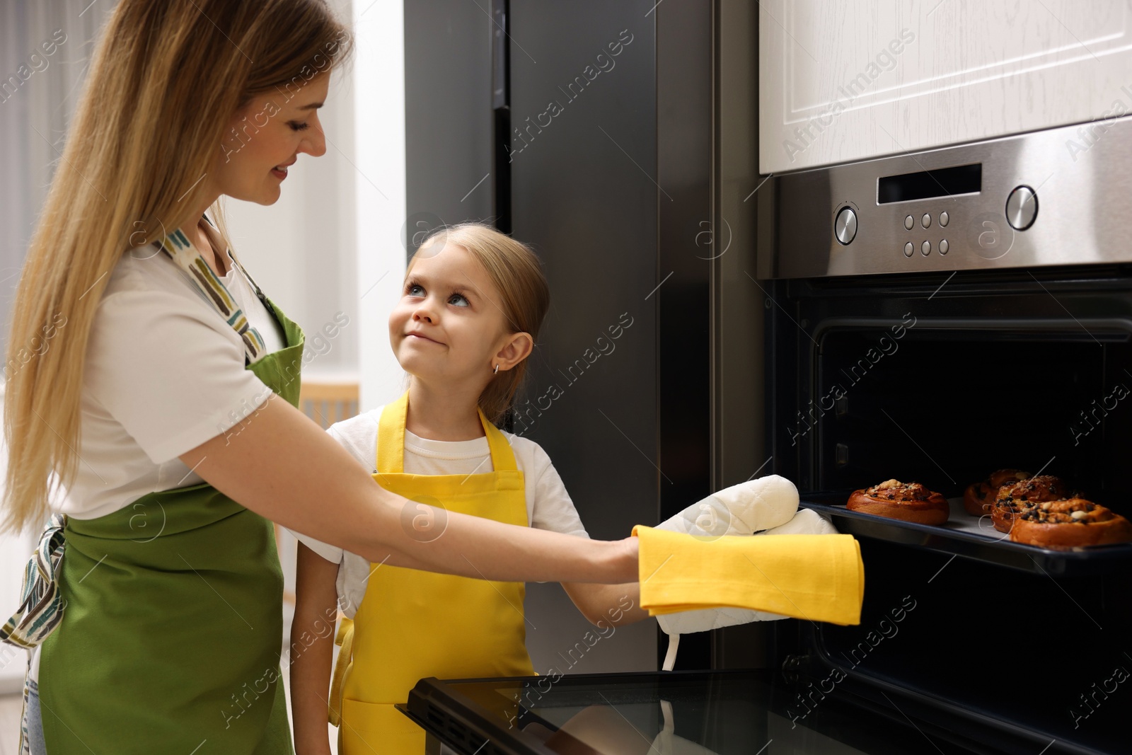 Photo of Mother and her daughter taking out buns from oven in kitchen