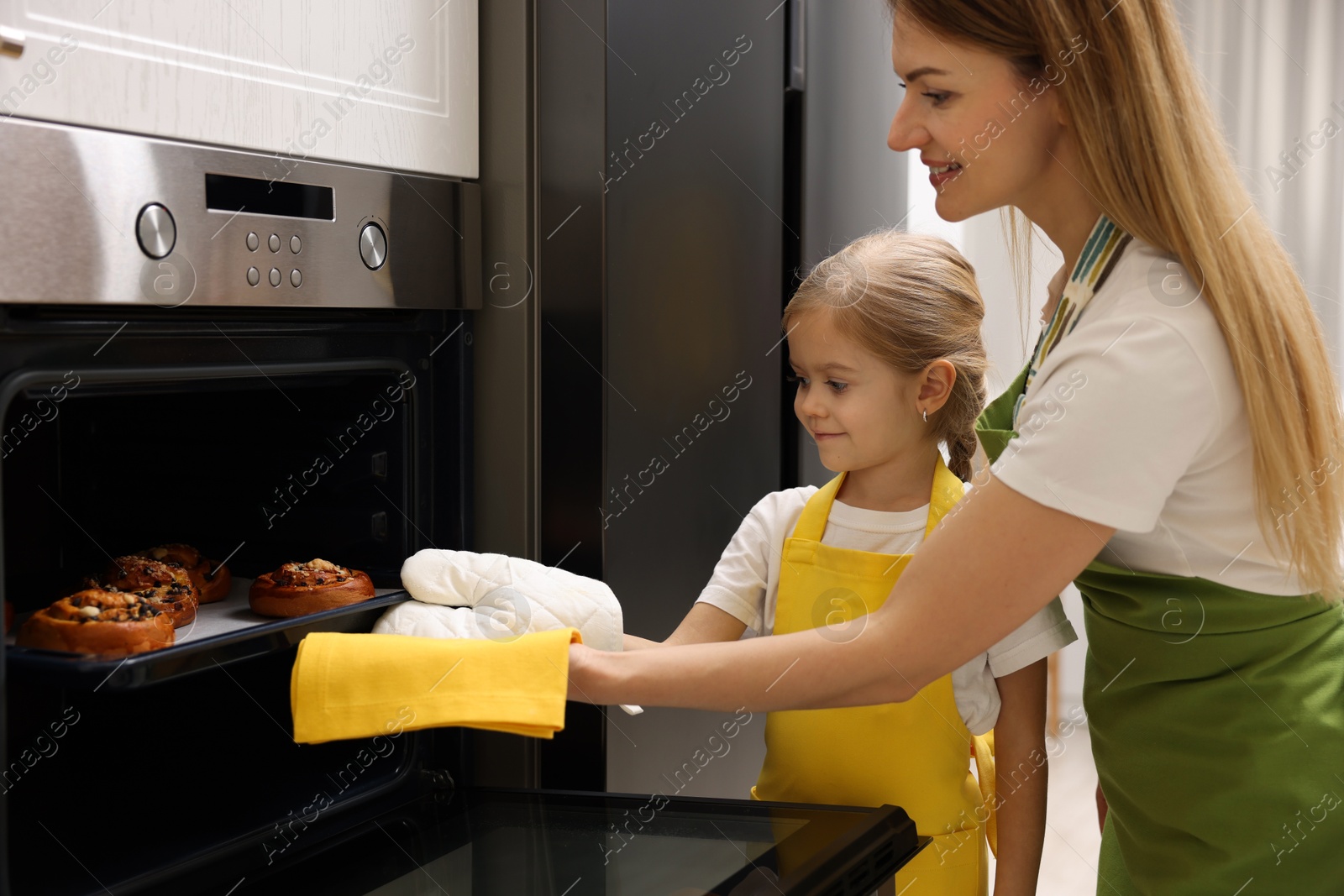 Photo of Mother and her daughter taking out buns from oven in kitchen