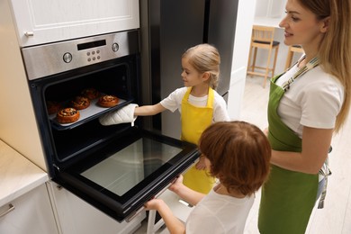 Photo of Mother and her kids taking out buns from oven in kitchen