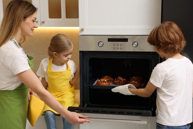 Photo of Mother and her kids taking out buns from oven in kitchen