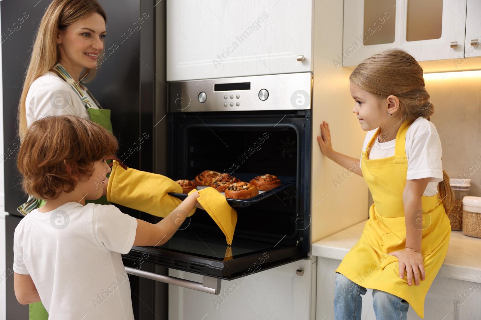 Photo of Mother and her kids taking out buns from oven in kitchen