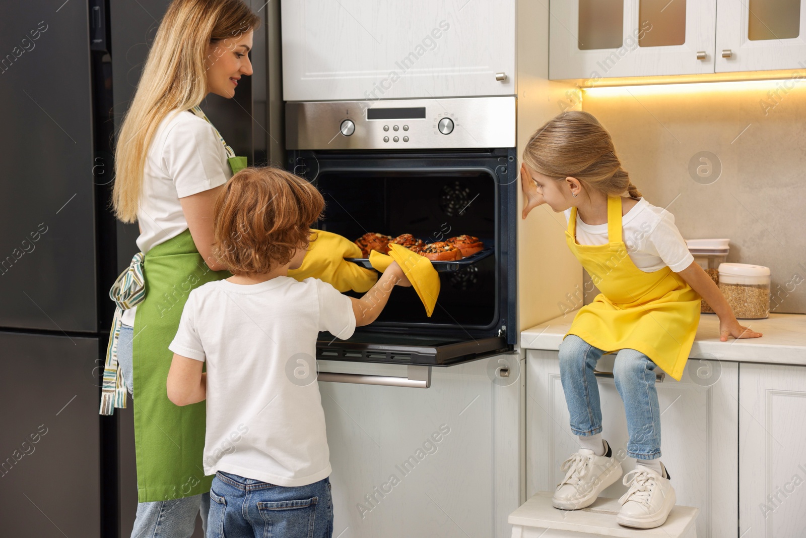 Photo of Mother and her kids taking out buns from oven in kitchen