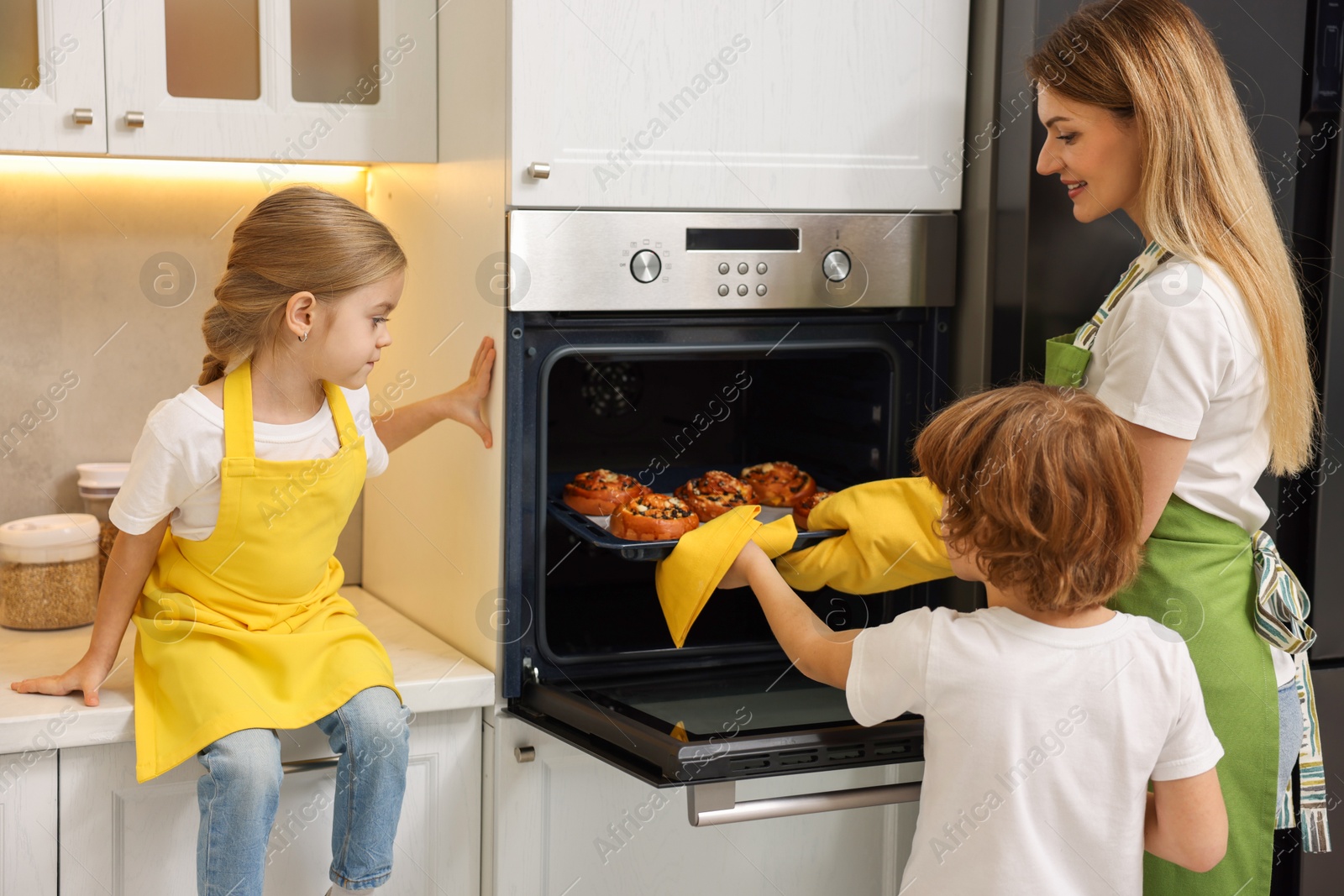 Photo of Mother and her kids taking out buns from oven in kitchen