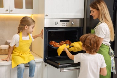 Photo of Mother and her kids taking out buns from oven in kitchen