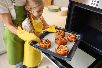 Photo of Mother and her daughter taking out buns from oven in kitchen, closeup