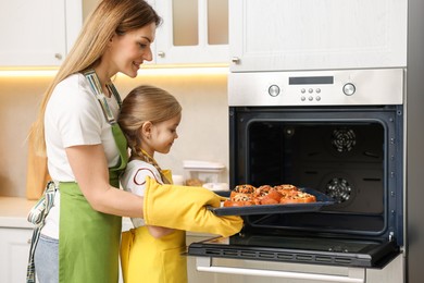 Photo of Mother and her daughter taking out buns from oven in kitchen