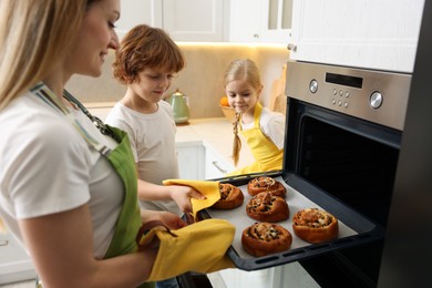 Photo of Mother and her kids taking out buns from oven in kitchen