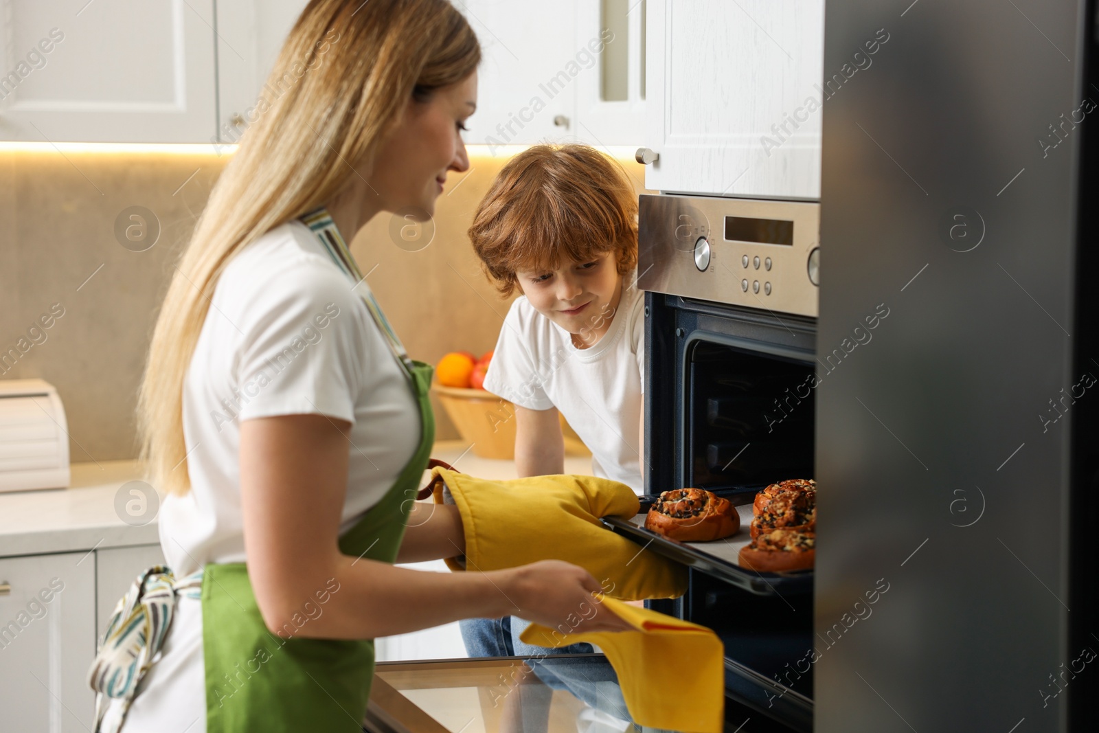 Photo of Mother and her son taking out buns from oven in kitchen